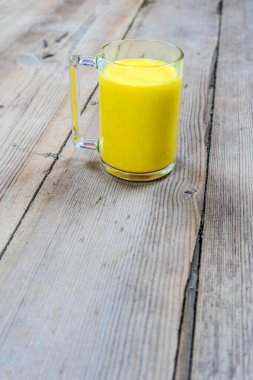 Tahta bir arka planda, cam bir fincandaki altın süt.