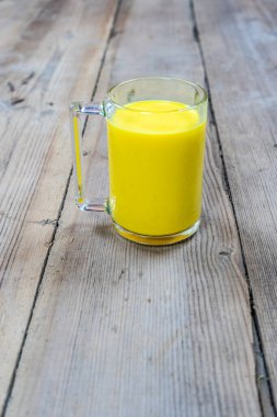 Tahta bir arka planda, cam bir fincandaki altın süt.