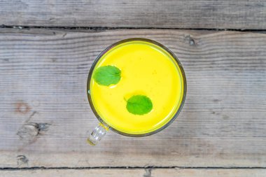 Tahta bir arka planda, cam bir fincandaki altın süt.