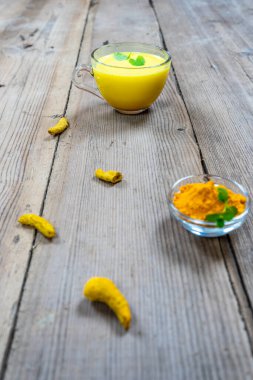 Tahta bir arka planda, cam bir fincandaki altın süt.