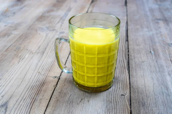 Golden milk in a glass cup on a wooden background — Stock Photo, Image