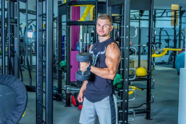 Yakışıklı ve kaslı bir adam, spor salonunda kameraya poz veriyor.