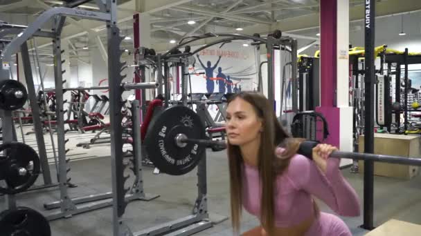 Jovencita alegre se pone en cuclillas con una barra en el gimnasio — Vídeo de stock