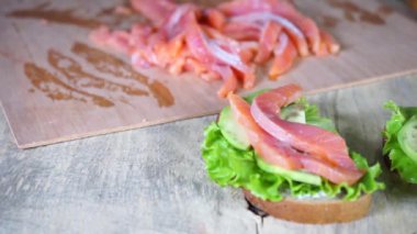 Ahşap bir yüzeyde avokado sandviçi, marul ve kırmızı balık.