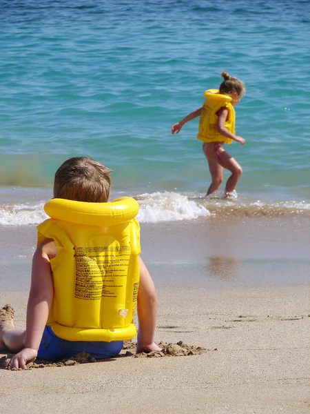 Los niños juegan en la playa en chaleco salvavidas —  Fotos de Stock