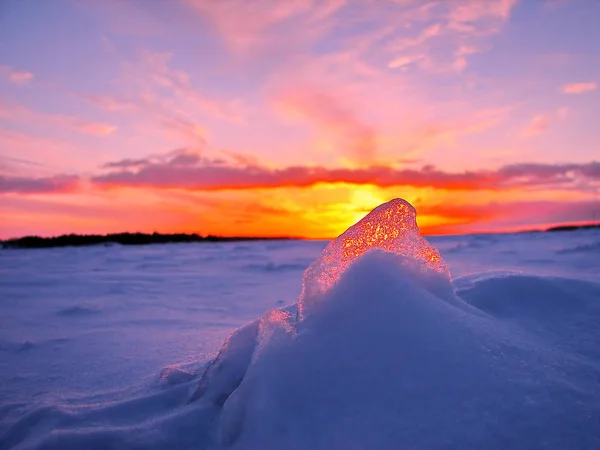 Transparante stuk ijs in de sneeuw tegen de achtergrond van een zonsondergang in de winter — Stockfoto