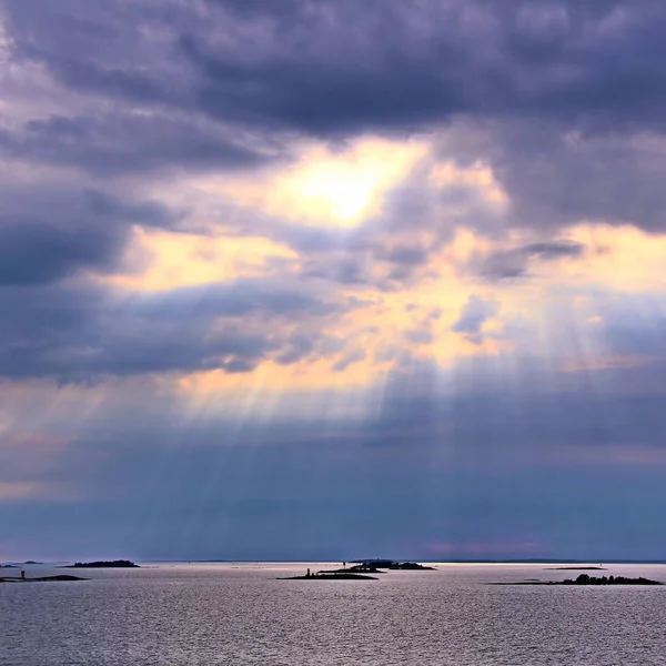 De zon achter de wolken met stralen van licht schijnt neer op zee — Stockfoto