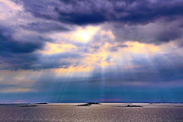 El sol detrás de las nubes con rayos de luz brillando en el mar — Foto de Stock
