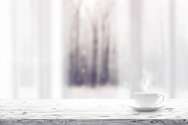 木製のテーブルと冬の雪に覆われた森の背景の上の窓にホットド リンクのカップ — ストック写真