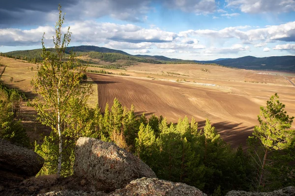 plowed field, arable land, among the rocks, blue sky with clouds, horizontal landscape