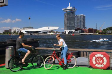AMSTERDAM, NETHERLANDS - 9 Temmuz 2017: bisikletçiler feribotun Amsterdam, Hollanda 'da IJ körfezinden geçmesini bekliyorlar. Amsterdam Hollanda 'nın başkentidir..