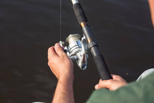 Fisherman catches a fish. Hands of a fisherman with spinning rod in hand close up