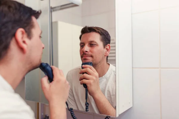 Morning hygiene, young man in mirror shaving with electric shave