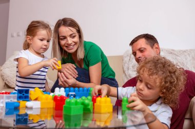 Oynak genç aile - genç gülümseyen erkek ve kadın evde çocuklarla oynarken