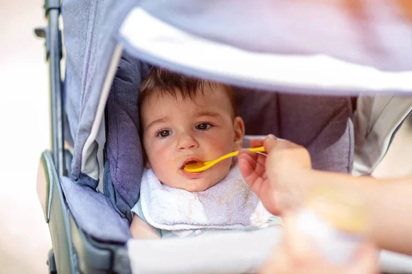 Adorable baby boy is eating while sitting in a baby carriage — Stock Photo, Image
