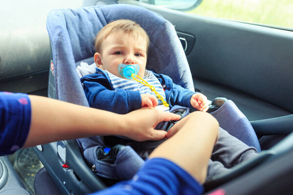 Protection in the car. woman is fastening security belt to child