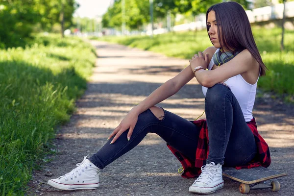 Sporty girl sitting on skateboard. Outdoors, urban lifestyle