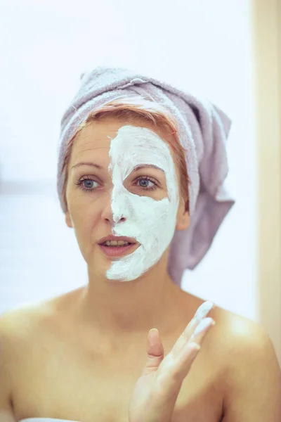 Улыбающаяся женщина надевает маску для лица. Косметические процедуры — стоковое фото