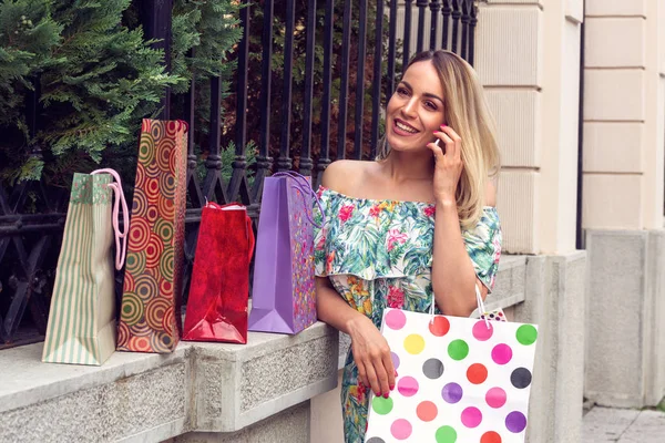 Femme tenant des sacs à provisions, utilisant un téléphone intelligent et souriant tout en restant debout à l'extérieur — Photo