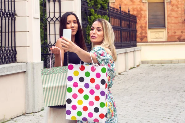 Dziewcząt posiadających torby na zakupy, za pomocą inteligentnego telefonu i uśmiechając się, stojąc na zewnątrz — Zdjęcie stockowe