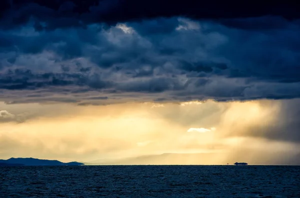 Puesta de sol sobre nubes tormentosas a través del agua reflejando el oscuro y dramático cielo sombrío —  Fotos de Stock