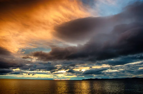 Puesta de sol sobre nubes tormentosas a través del agua reflejando el oscuro y dramático cielo sombrío —  Fotos de Stock