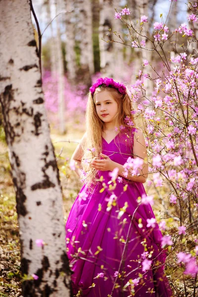 Un enfant se tient au milieu du lédum et du bouleau dans une robe rose et souriant — Photo