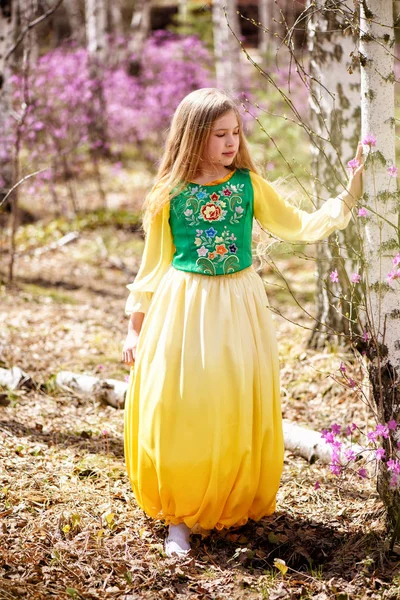 Ein Kind steht zwischen Ledum und Birke in grün-gelbem Kleid und lächelt — Stockfoto