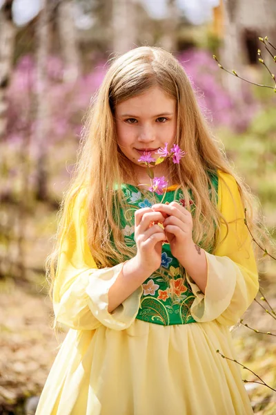 Un enfant se tient au milieu du lédum et du bouleau en robe jaune verte et souriant — Photo