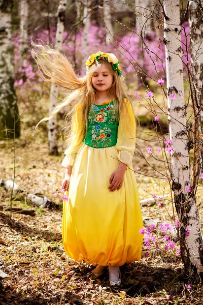 Un enfant se tient au milieu du lédum et du bouleau en robe jaune verte, souriant et coiffé à la mouche — Photo