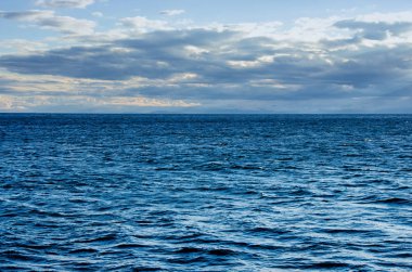 Bulutlu gökyüzü ile su yüzeyindeki dalgalar. Derin mavi renk