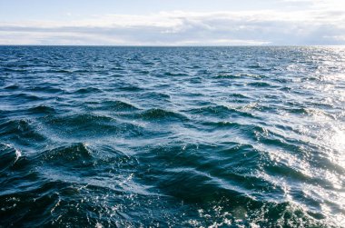 Bulutlu gökyüzü ile su yüzeyindeki dalgalar. Derin mavi renk