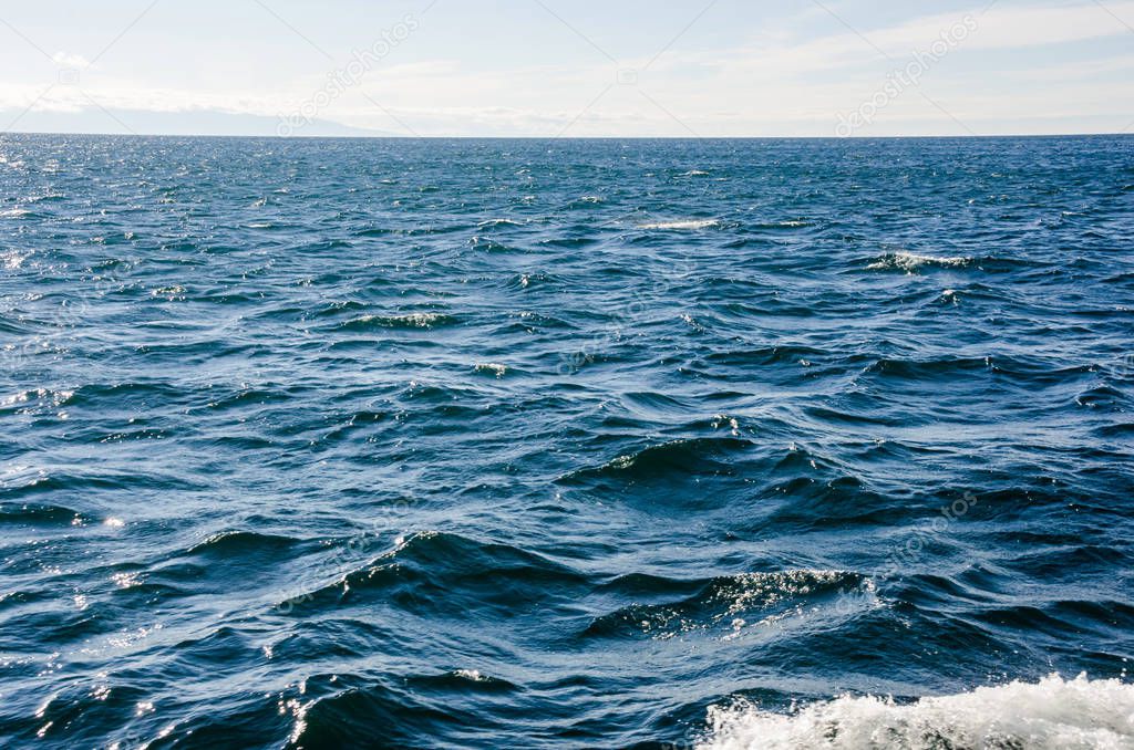 Waves on surface of water with cloudy sky. Deep blue color