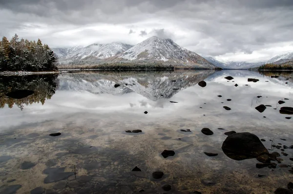 Bergsee Froliha, Kiefer und Steine über transparentes Wasser mit Schnee am Spiegelsee — Stockfoto