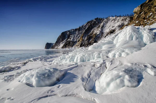 Lago Baikal está cubierto de hielo y nieve, fuerte frío, hielo azul claro grueso. Icicles cuelgan de las rocas. El lago Baikal es un día helado de invierno. Increíble lugar — Foto de Stock