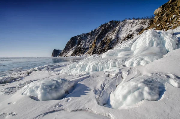 Lake Baikal is covered with ice and snow, strong cold, thick clear blue ice. Icicles hang from the rocks. Lake Baikal is a frosty winter day. Amazing place Stock Photo