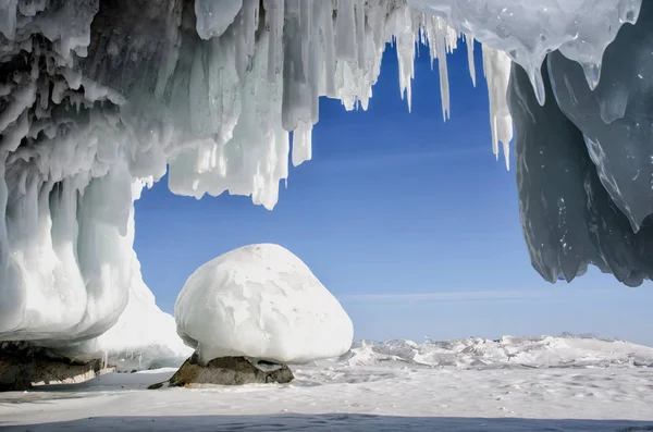 Blue white ice cave with icicle stalactites, blue sky and stone covered ice — Stock Photo, Image