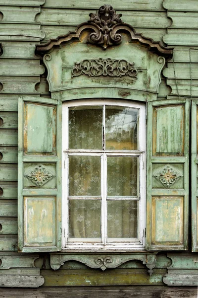 Window with the wooden carved architrave in the old wooden house in the old Russian town. — Stock Photo, Image