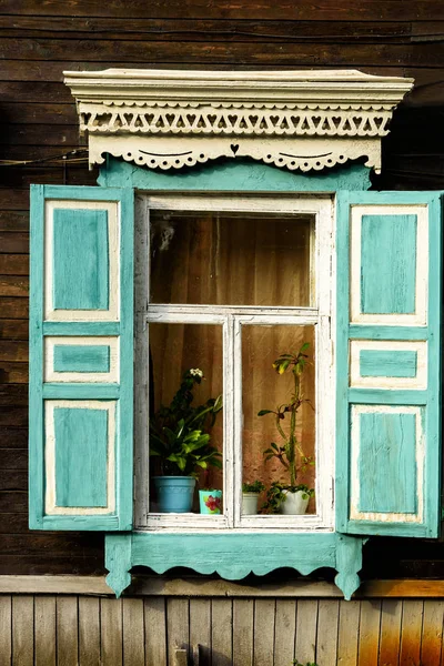 Window with the wooden carved architrave in the old wooden house in the old Russian town. — Stock Photo, Image