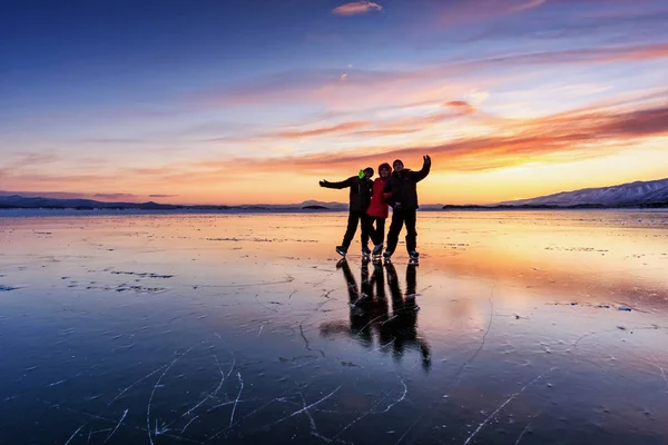 Россия, Сарма - 3 января 2019 года: Три человека на коньках стоят на льду озера Байкал и веселятся на светло-оранжевом желтом закате зимнего вечера. Наслаждайтесь спортом в холодную погоду . — стоковое фото