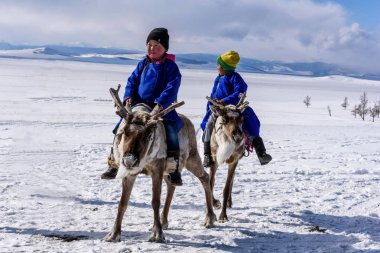 Hatgal, Mongolia, Febrary 25, 2018: Little tsaatan boys in traditional Mongolian riding on reindeers. clipart