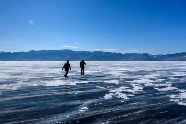 Frozen Lake Baikal. Two people silhouettes walk on the ice surface on a frosty day with beautiful mountain. Natural background