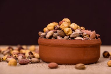 Badem, antep fıstığı, fındık ve yuvarlak fındık dokulu kahverengi ve açık arka plan üzerinde kase. Tablo görünümü gıda.