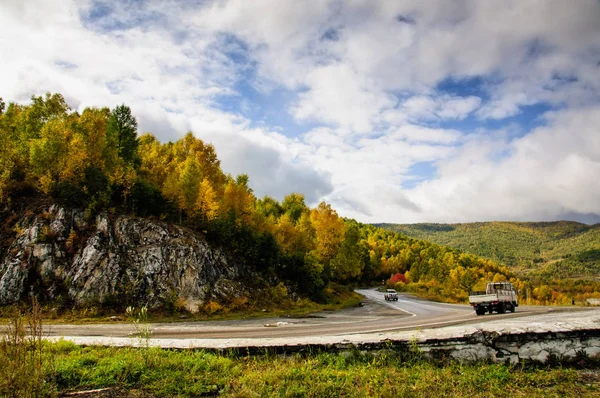 Un camino curvo de otoño con coloridos bosques y montañas en la lejana distancia — Foto de Stock