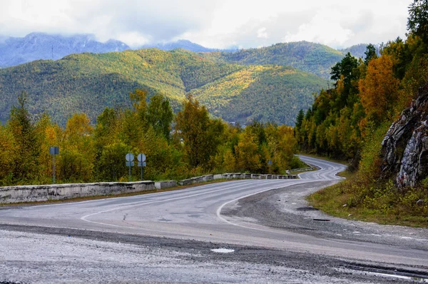 Un camino curvo de otoño con coloridos bosques y montañas en la lejana distancia — Foto de Stock