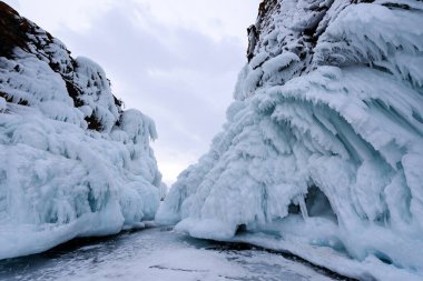 Buz saçaklarıyla kaplı iki taş. Baykal Gölü bulutlu bir havada. Adanın güney burnu Olkhon Mares 'in başı