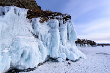 Buz saçaklarıyla kaplı kaya. Baykal Gölü bulutlu bir havada.