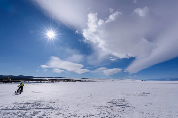 Silhouette of man rides bicycle on the frozen lake Baikal in sunny weather with beautiful clouds sky
