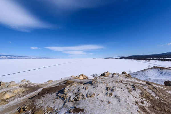 Pohled na pláž Sarai od mysu Burhan na ostrově Olkhon za slunečného zimního dne. Zmrzlé jezero Bajkal pokryté sněhem. Krásné stratus mraky nad ledovým povrchem v mrazivý den. — Stock fotografie