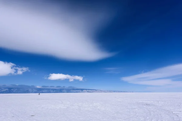 Silhouette of man rides bicycle on the frozen lake Baikal in sunny weather with beautiful clouds sky